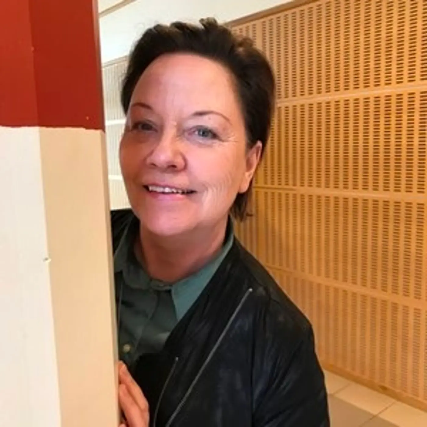 Porträttbild på en leende kvinna med kort hår som tittar fram bakom en pelare.