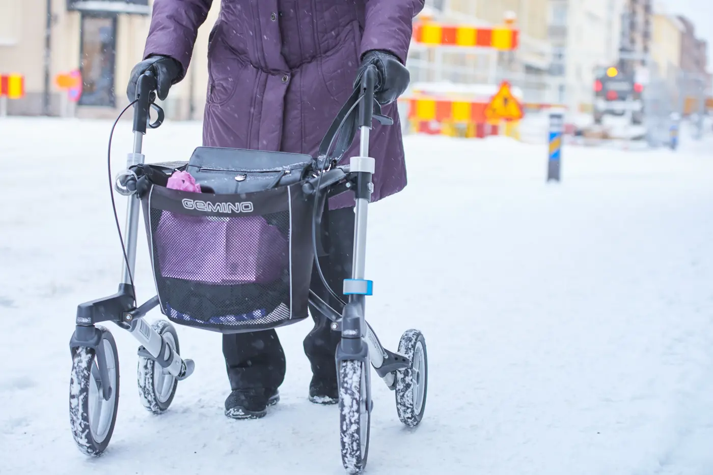 En äldre person promenerar i vintermiljö med en rollator.