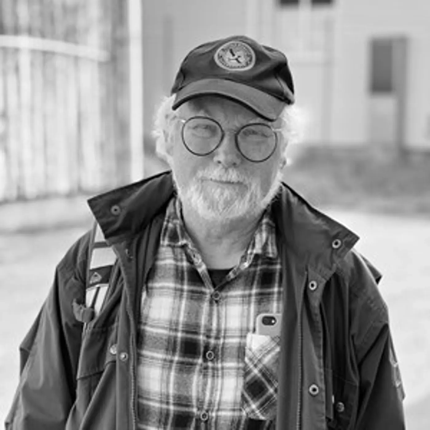 Svartvit porträttbild på en äldre man med glasögon och keps.