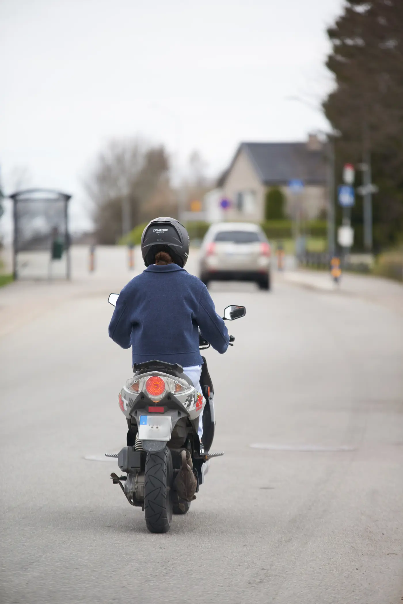 En ungdom kör moped på en asfalterad väg. Bilden är tagen bakifrån.
