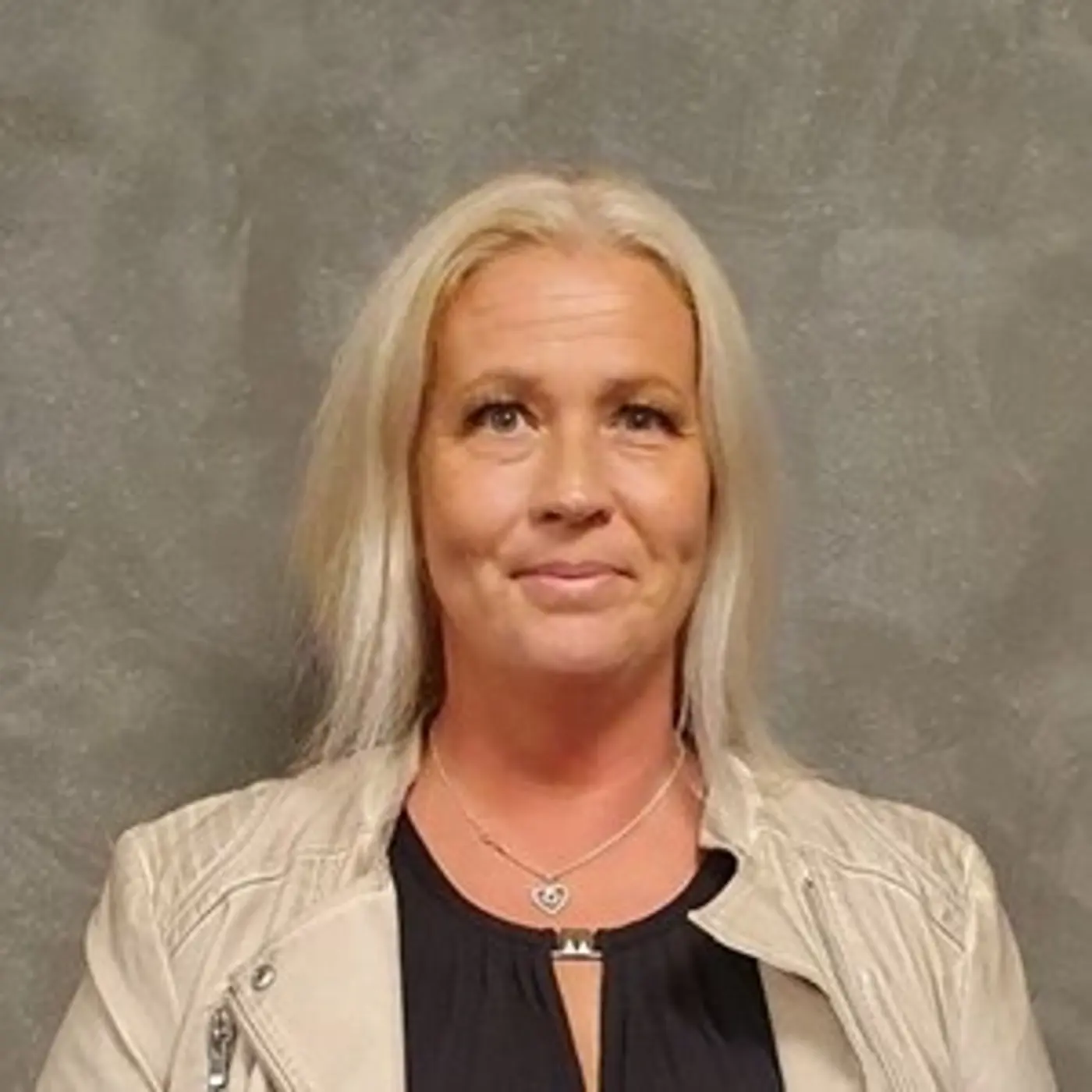 Porträttbild på en leende kvinna med blont hår och ljus skinnjacka.