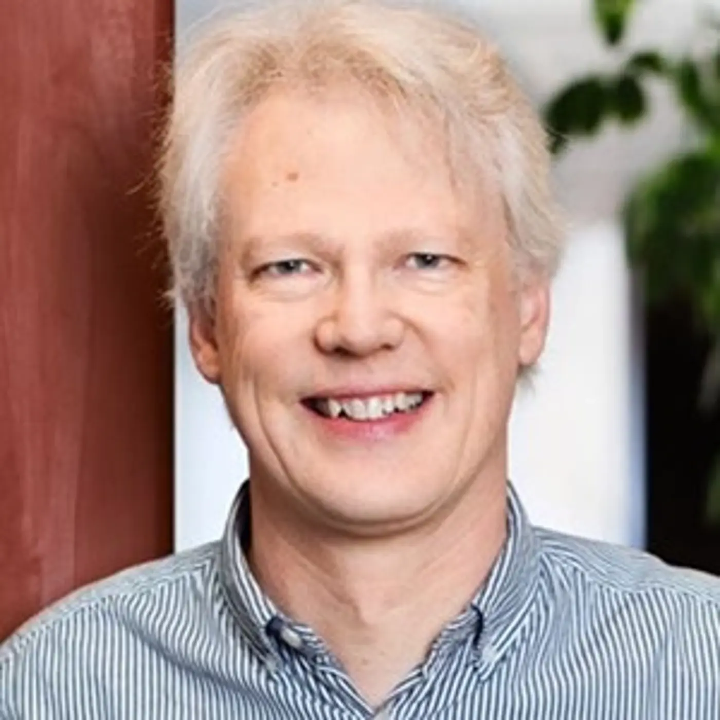 Porträttbild på en leende man med blå-vitrandig skjorta.