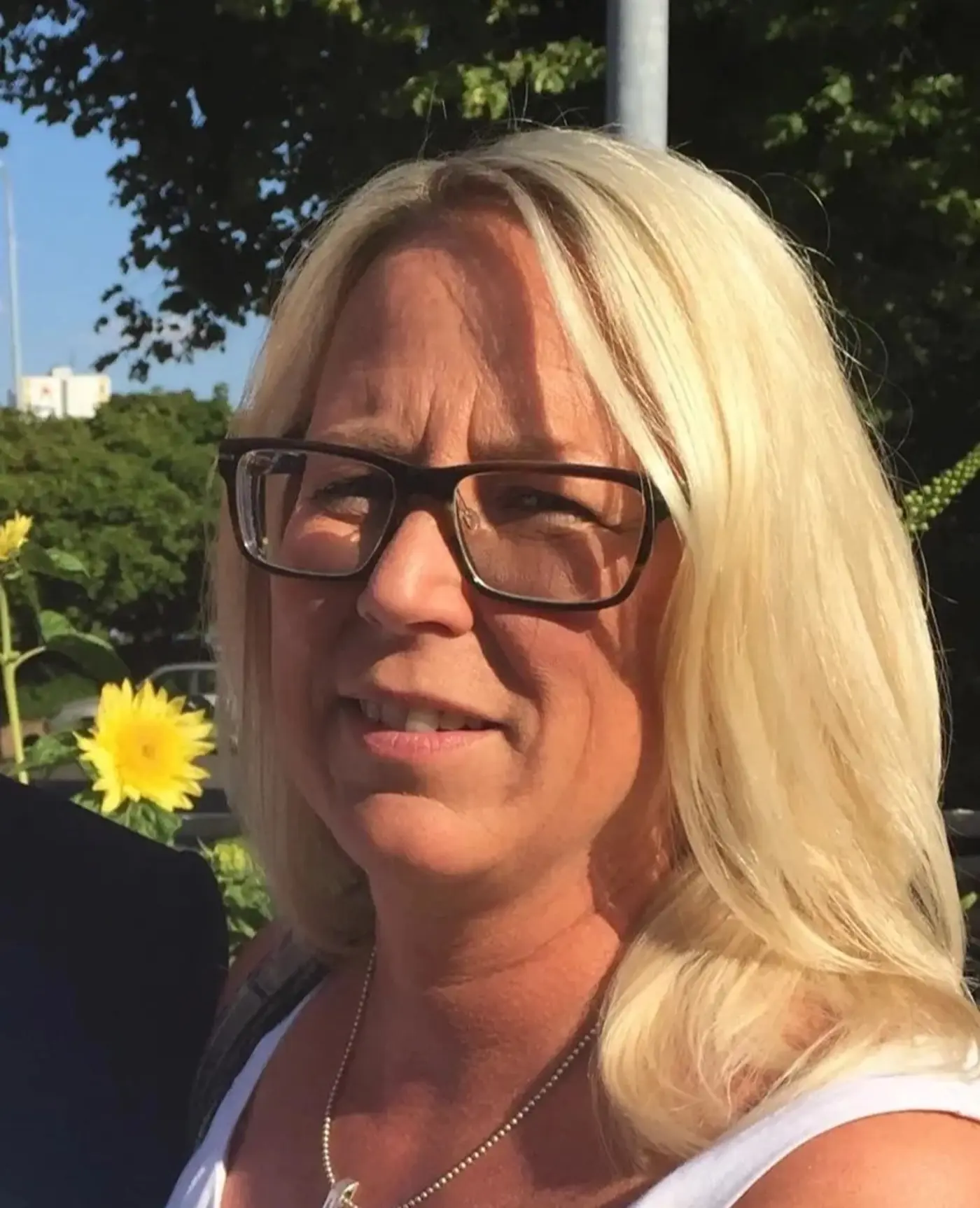 Porträttbild på en kvinna med blont hår som står ute i solen.