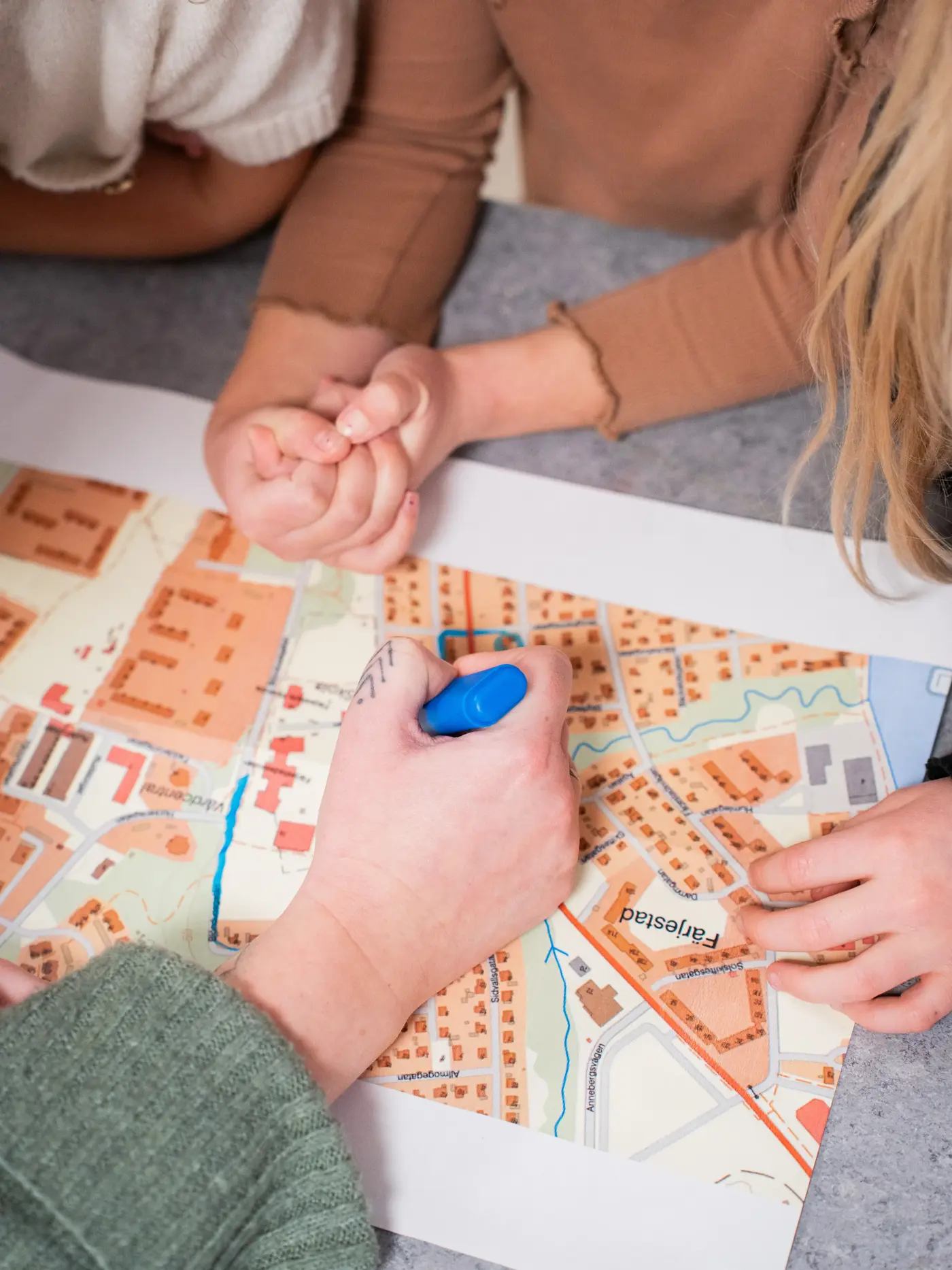 En karta ligger på ett bord och tre barn samt en lärare pekar på och markerar olika platser.