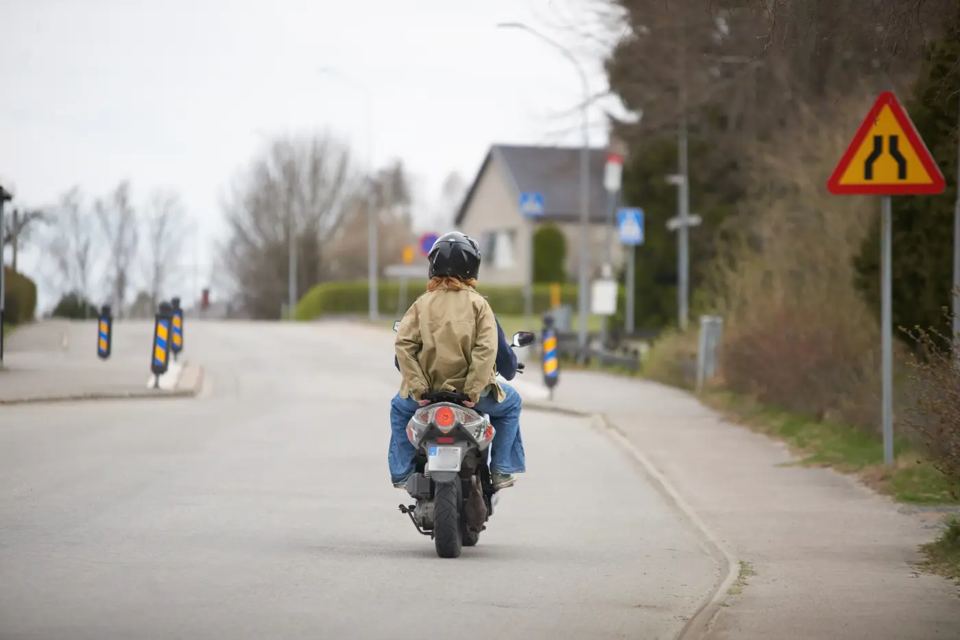 En ungdom skjutsar en annan ungdom på en moped. Bilden är tagen bakifrån.