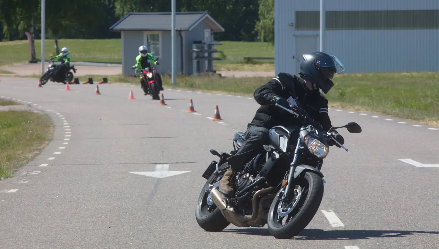 Tre personer på varsin motorcykel kör en slalombana av koner.