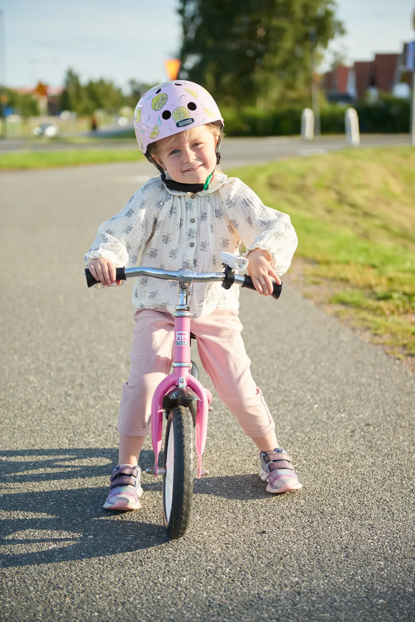 Ett småbarn sitter på en balanscykel och har en hjälm med grönt spänne på huvudet