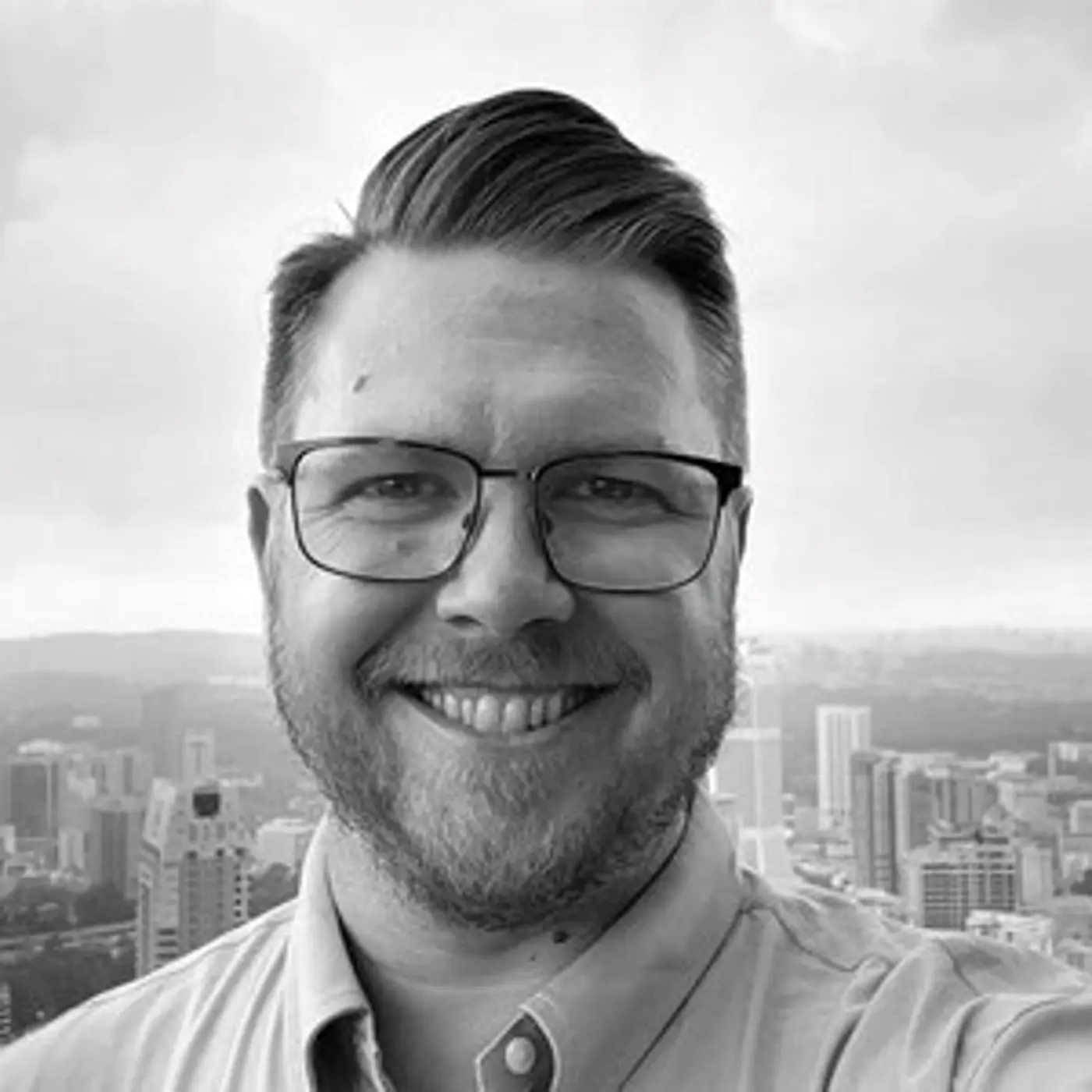 Svartvit porträttbild på en leende man med glasögon.