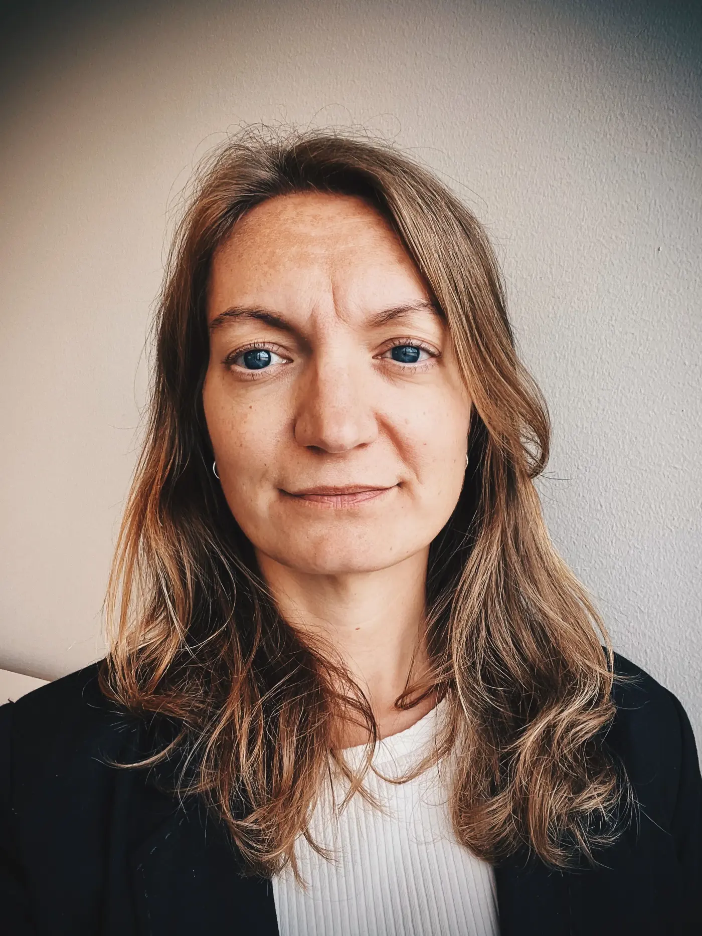 Porträttbild på en kvinna med brunt, vit ribbad tröja och svart kavaj.