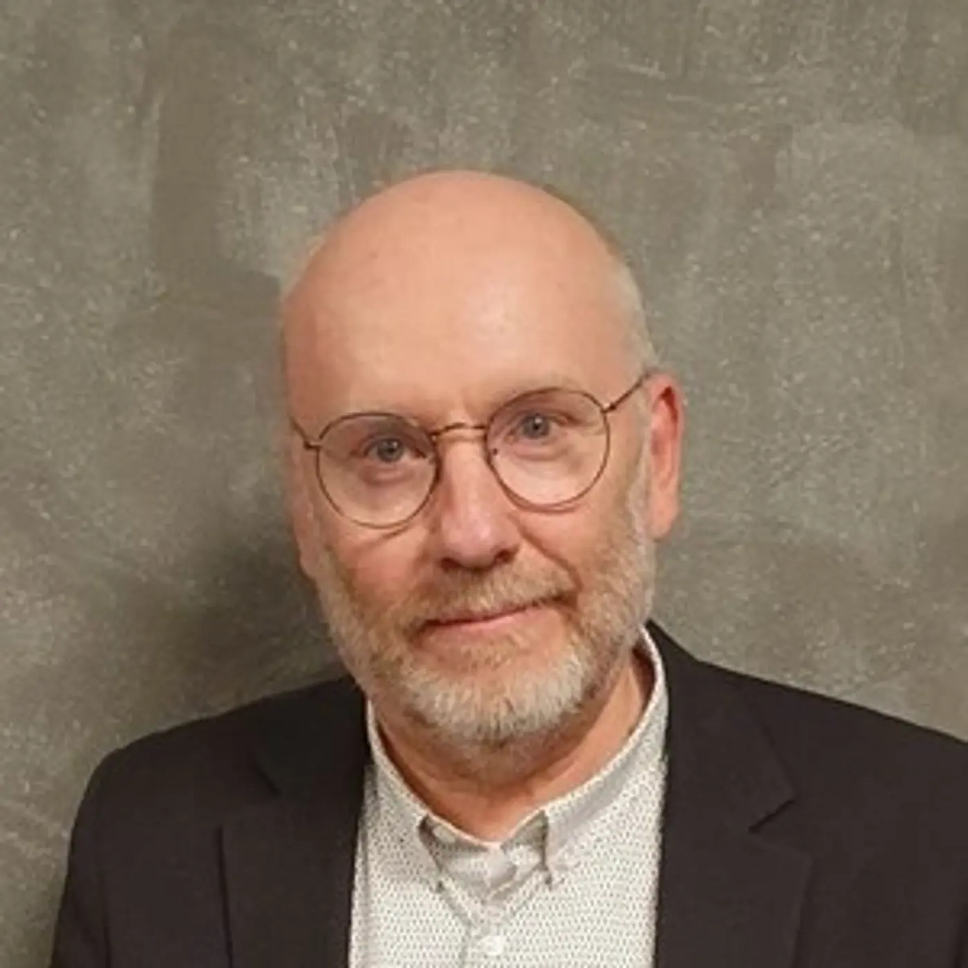 Porträttbild på en man med glasögon, skjorta och kavaj.