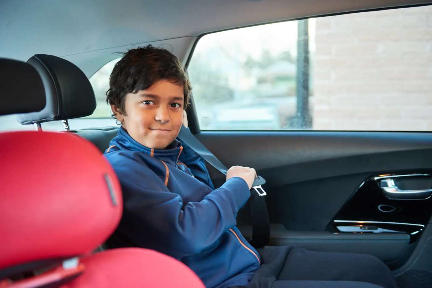 Ett barn sitter på en bälteskudde i baksätet och håller på att spänna fast säkerhetsbältet.