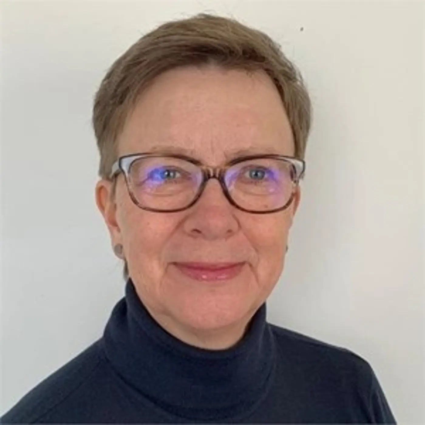 Porträttbild på en leende kvinna med glasögon och mörk polotröja.