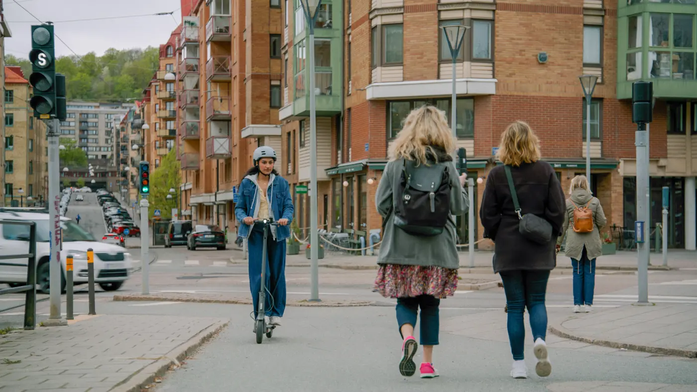 En ung kvinna med hjälm på huvudet kör elsparkcykel i stadsmiljö.