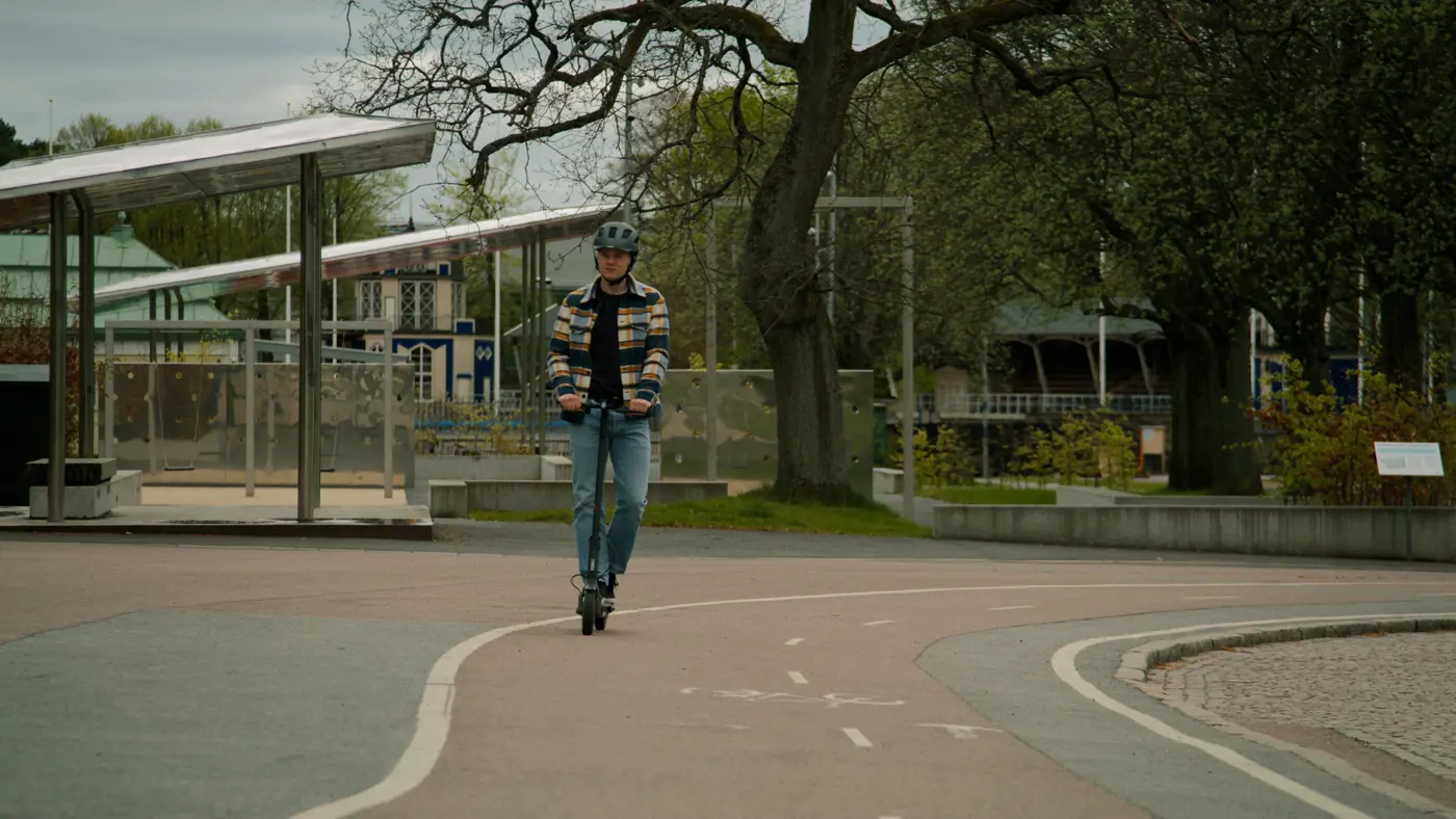 En ung vuxen kör elsparkcykel på en cykelbana. Han har hjälm på huvudet.