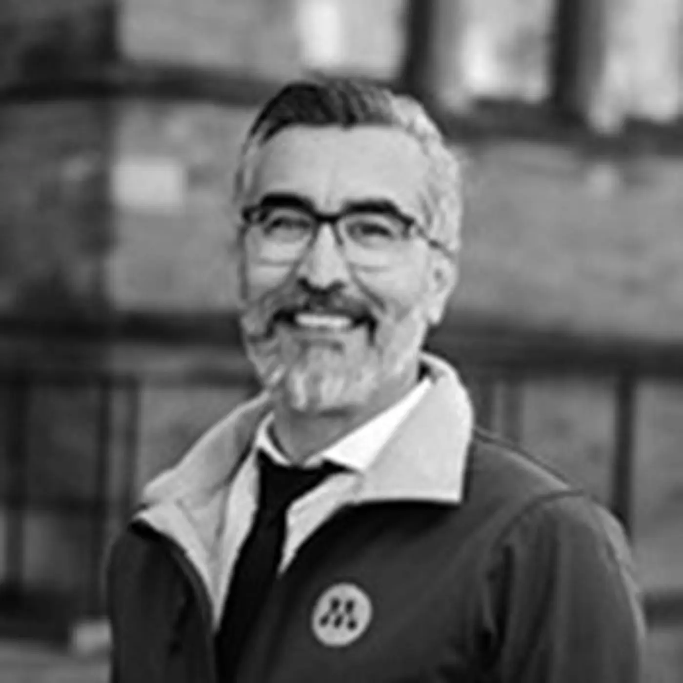 Svartvit porträttbild på en leende man med glasögon och skägg.