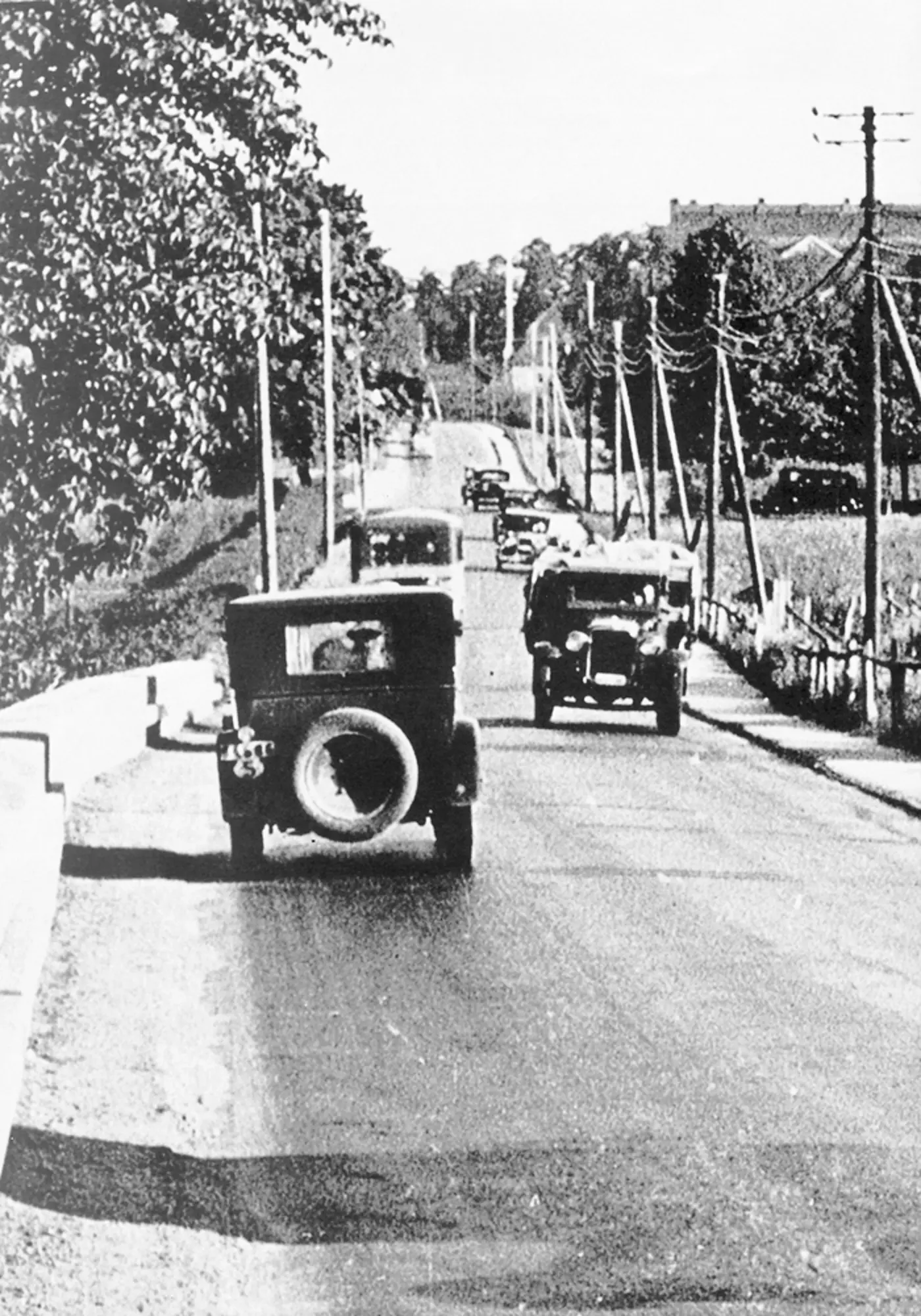 En gammal bild i svartvitt som visar en väg med bilar.