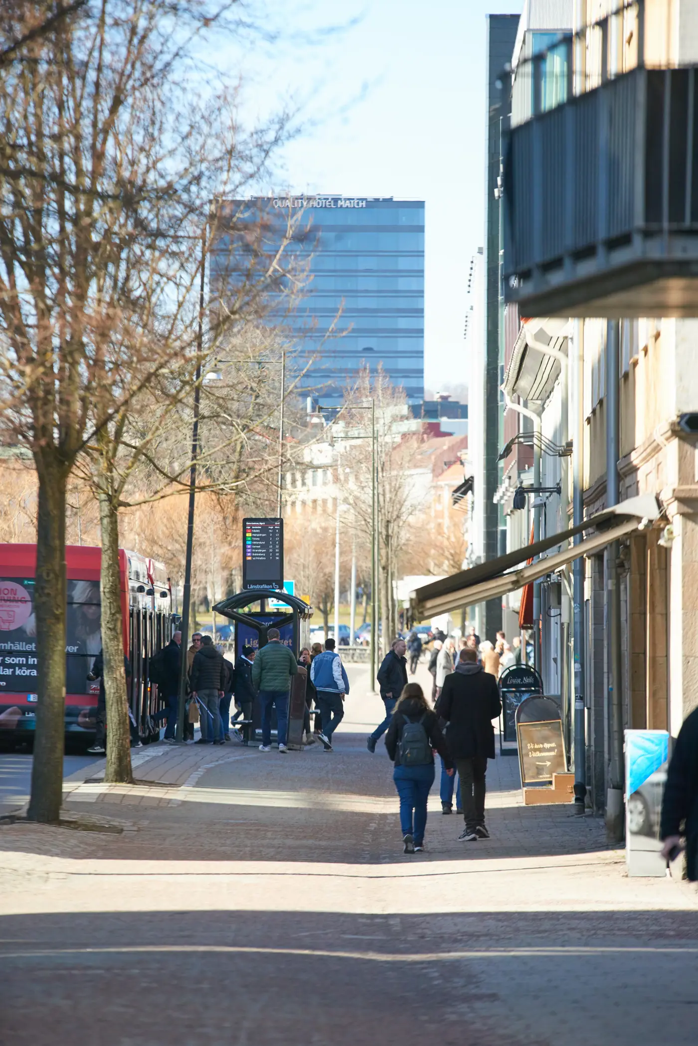 En gata med affärer, personer som går och en busstation där en buss står