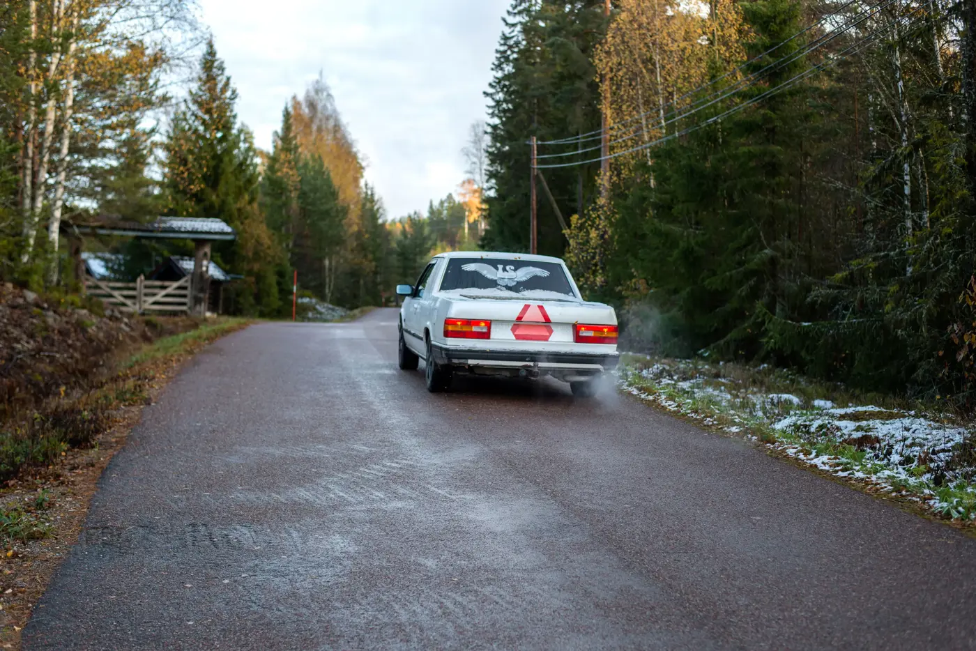 A-traktor kör på asfaltsväg i skogsmiljö.