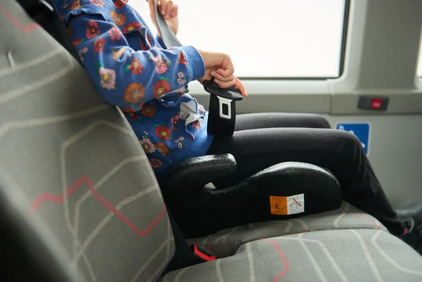 Ett barn sitter på en bälteskudde i en buss och spänner fast säkerhetsbältet.