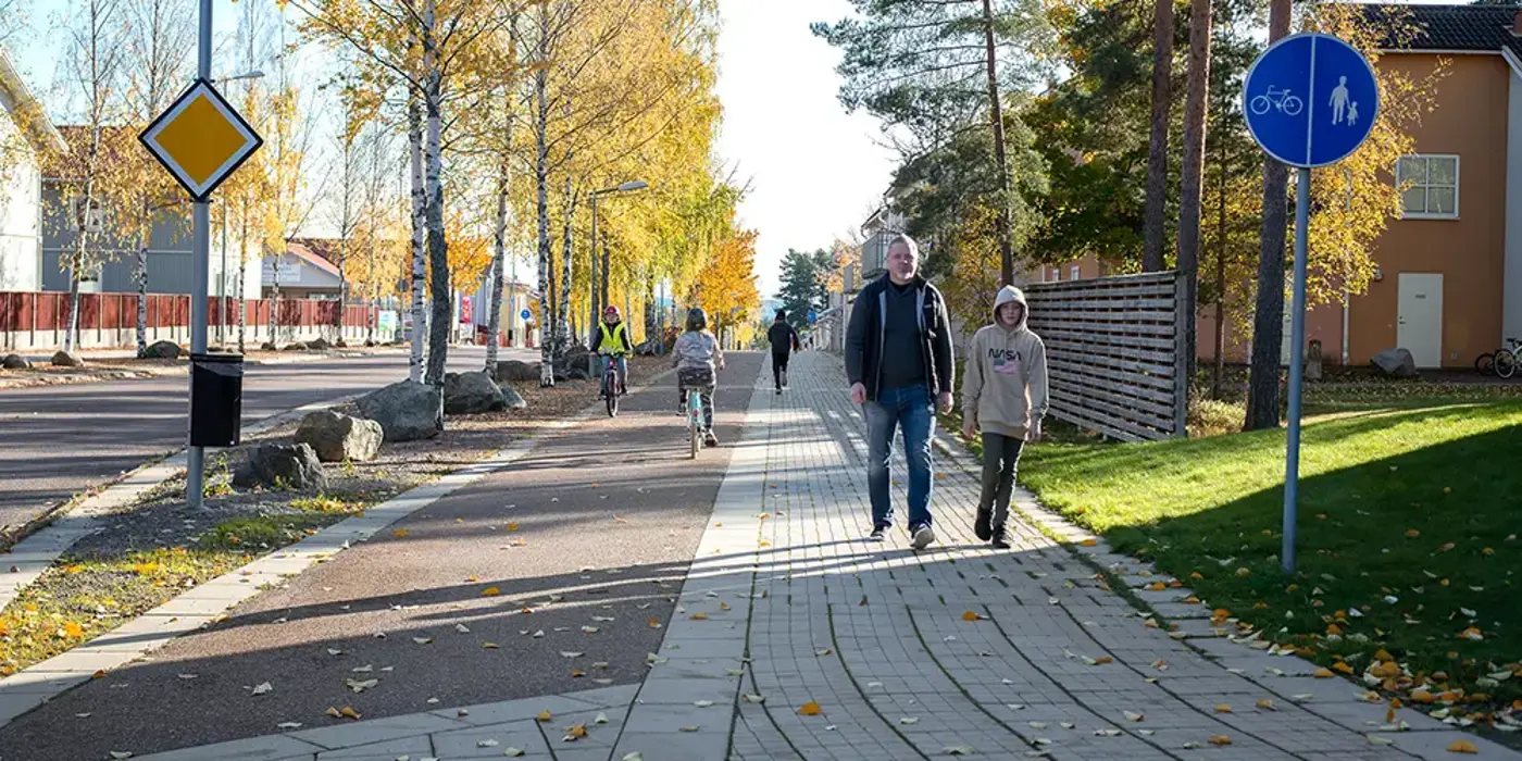 En vuxen och ett barn kommer gåendes på en gång-och cykelbana, i bakgrunden syns cyklister.
