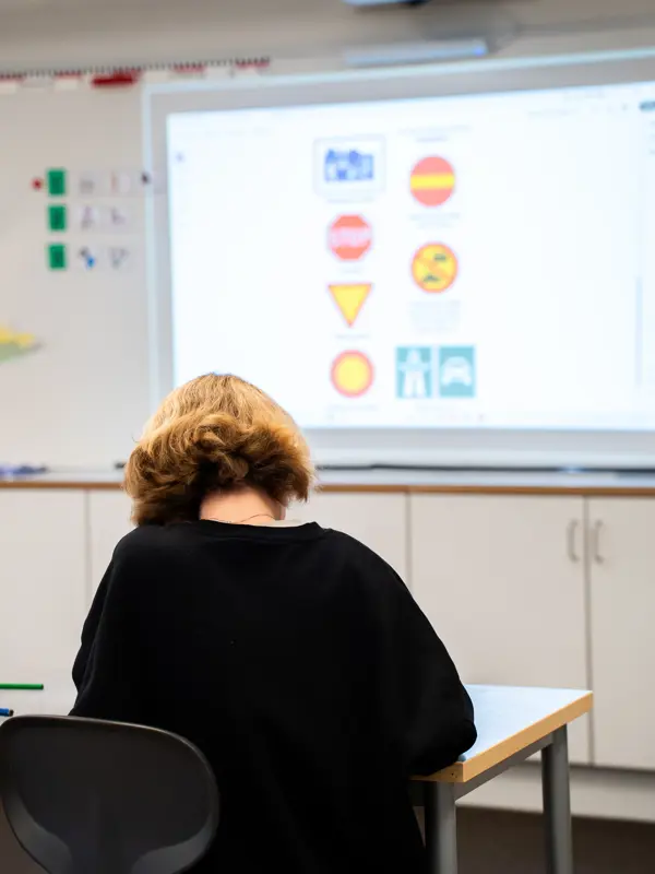 Ett skolbarn sitter i en skolbänk framför en tavla med en bild på olika vägmärken.