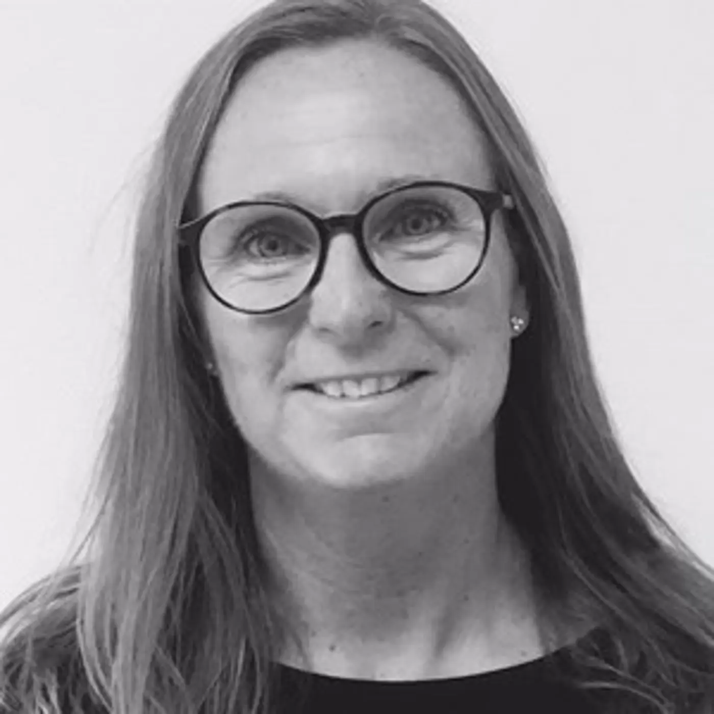 Svartvit porträttbild på en leende kvinna med långt hår och glasögon.