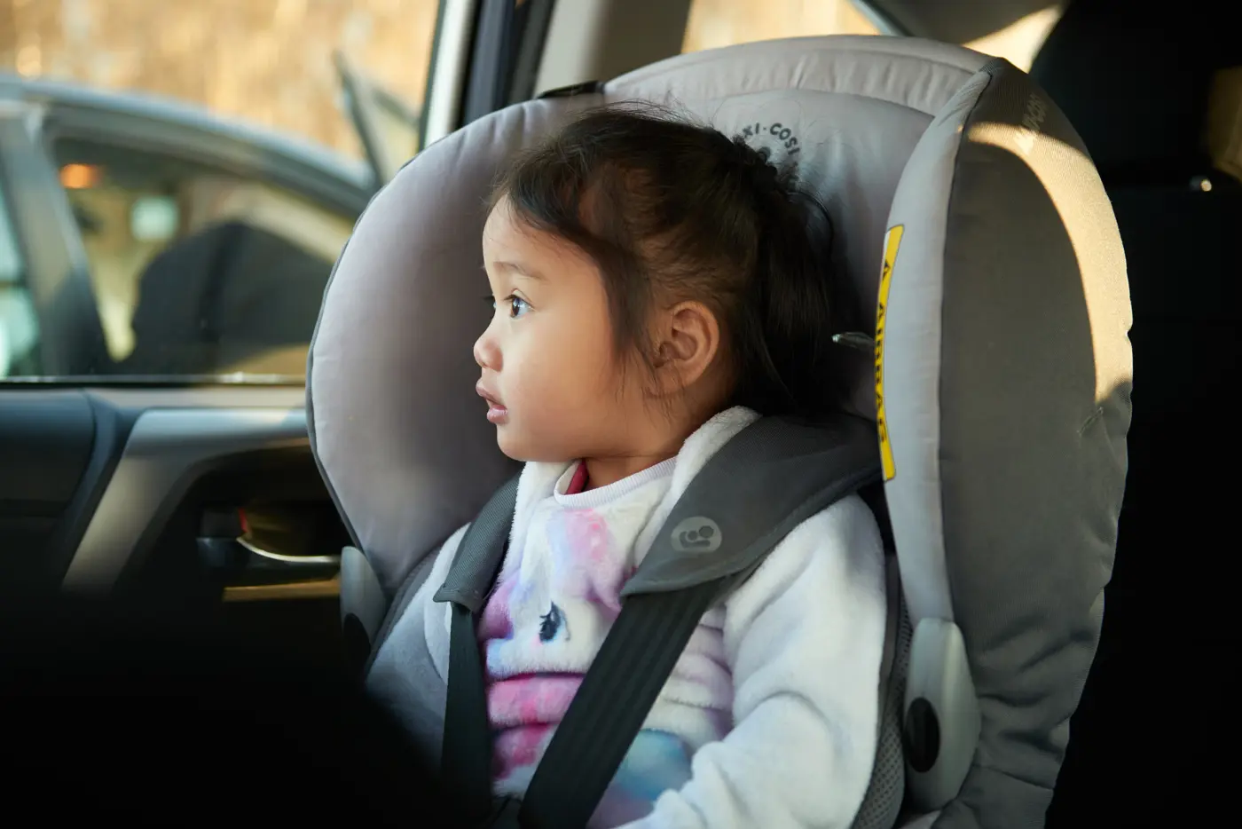 Ett småbarn sitter i en bakåtvänd bilbarnstol och tittar ut genom bilfönstret.