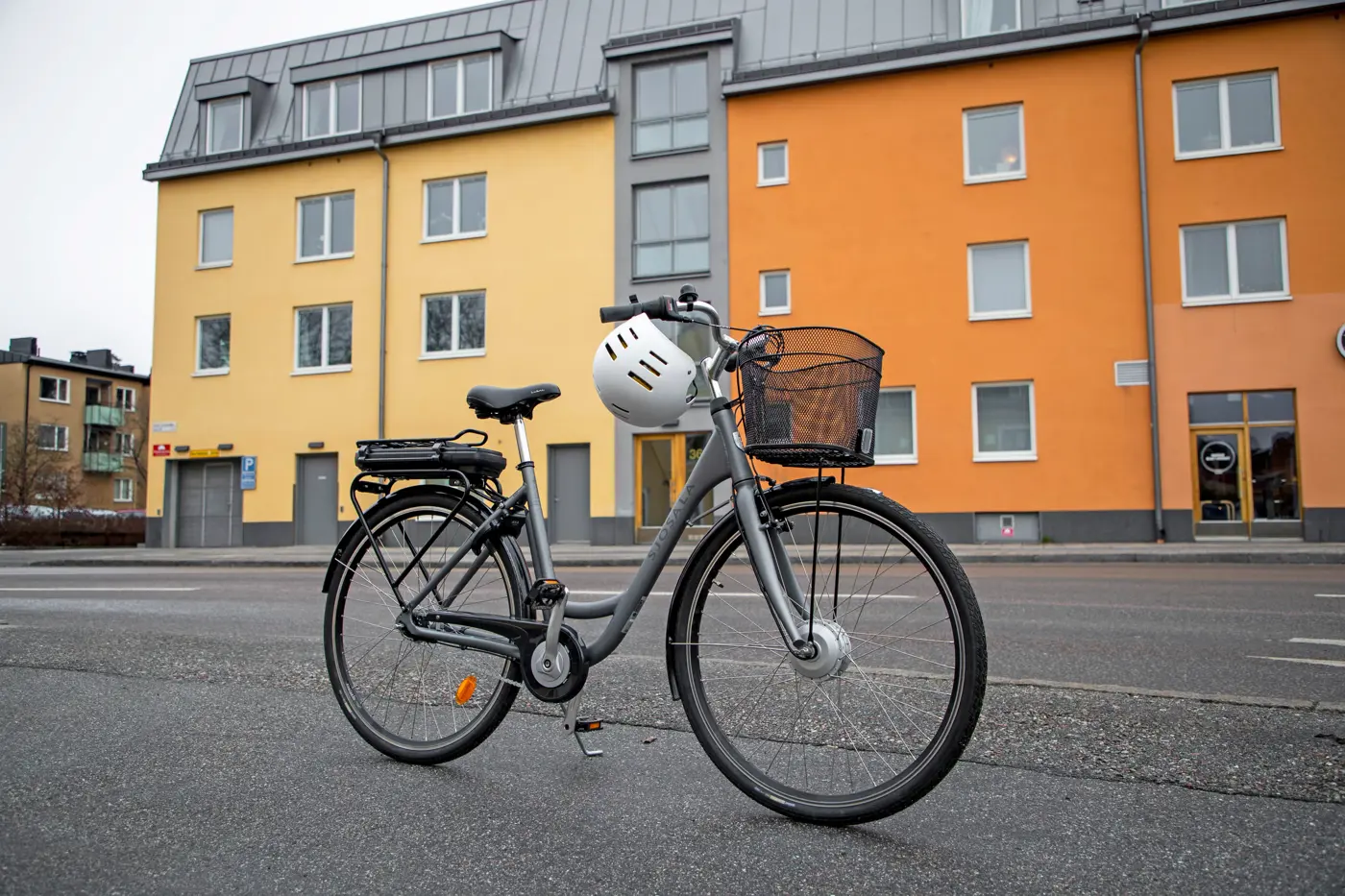 En elcykel står uppställd på gatan och på styret hänger en hjälm.