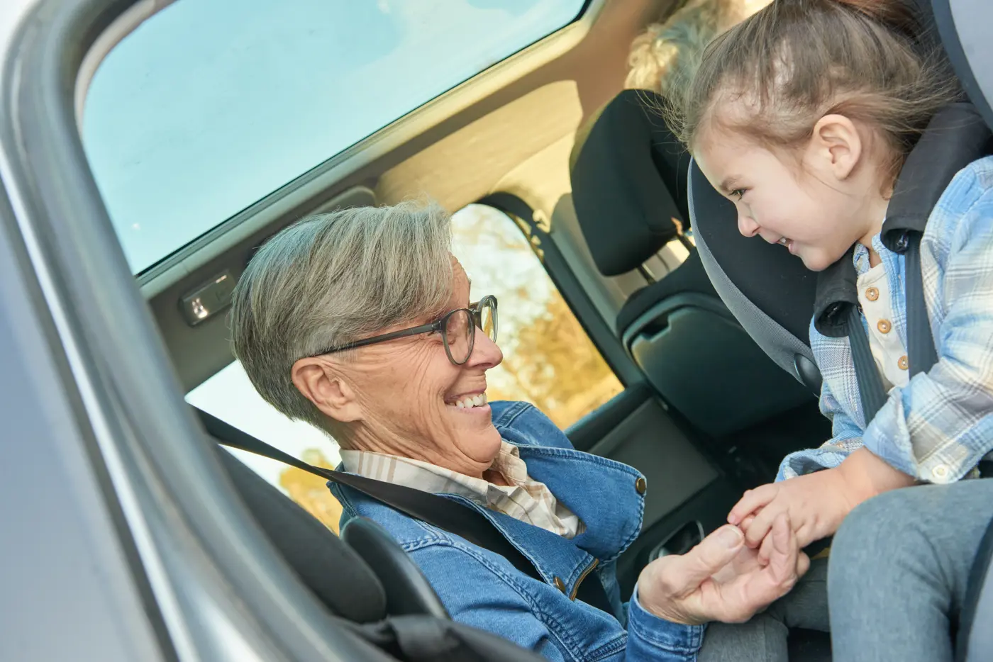 En äldre kvinna sitter med ett småbarn bredvid sig i baksätet på en bil. De skrattar tillsammans.