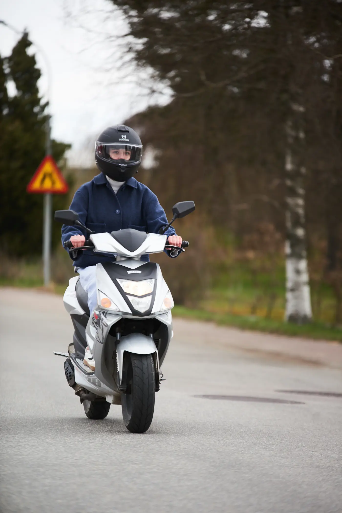 En ungdom kör moped på en asfalterad väg.