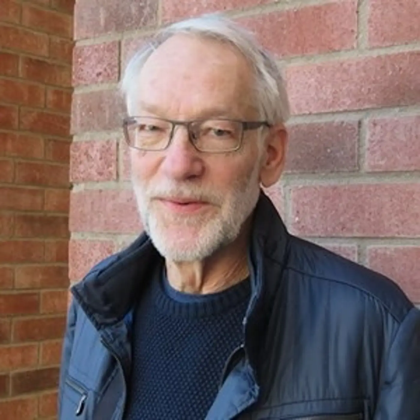 En porträttbild på en äldre man med kort vitt skägg och glasögon.