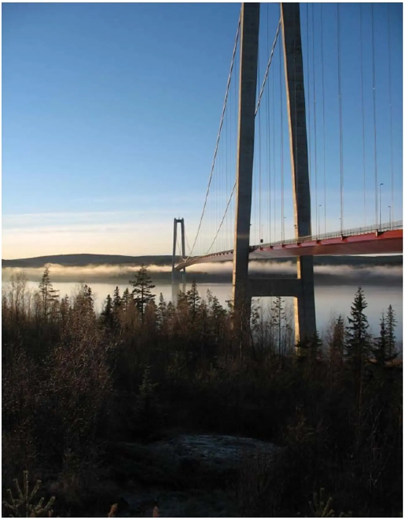 Högakustenbron i solnedgång med dimma som svävar en bit över vattenytan.
