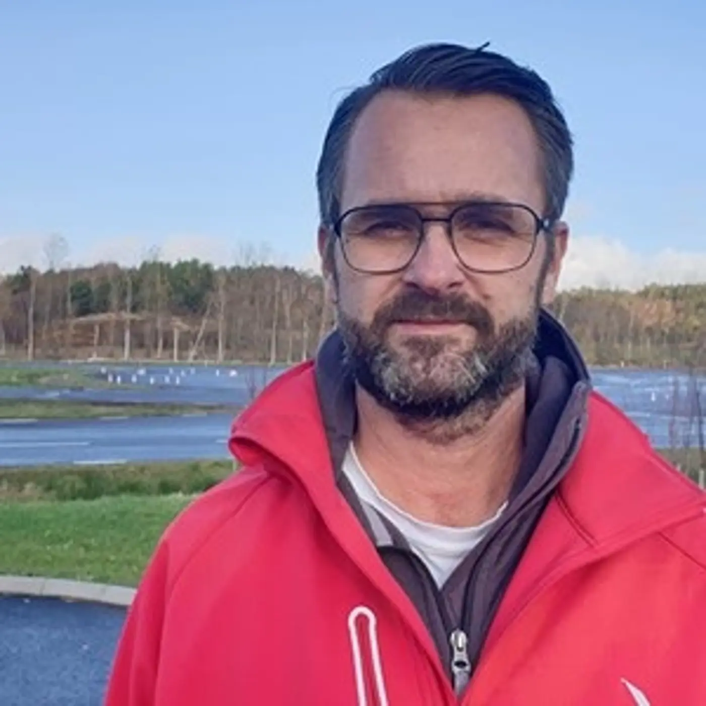 Porträttbild på en man med glasögon och röd jacka.