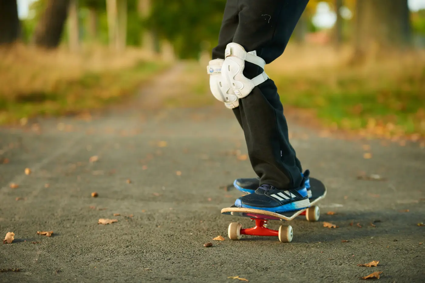Närbild på ett barn med knäskydd som kör skateboard på en asfalterad väg.