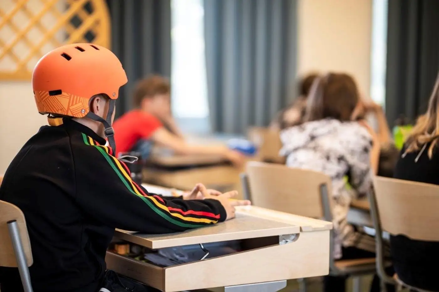 Barn som sitter i ett klassrum och en elev har en orange cykelhjälm på huvudet.