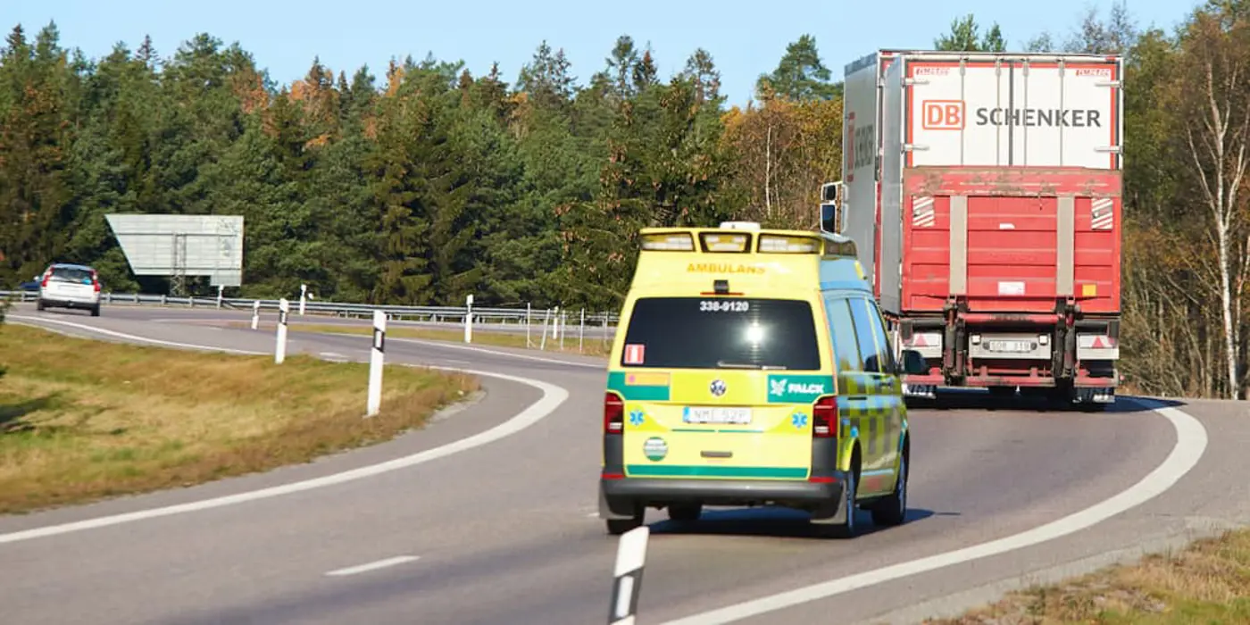 Bild av en ambulans som kör på bilväg bakom en lastbil