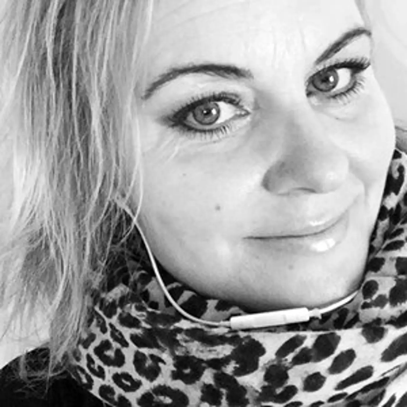 Svartvit porträttbild på en leende kvinna med kort hår och leopardmönstrad scarf.
