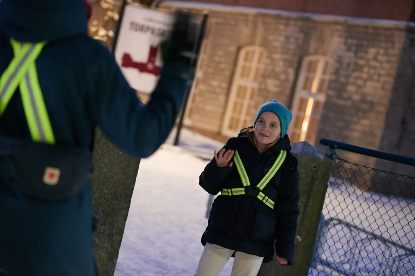 Ett barn med reflex och vinterkläder som vinkar. 
