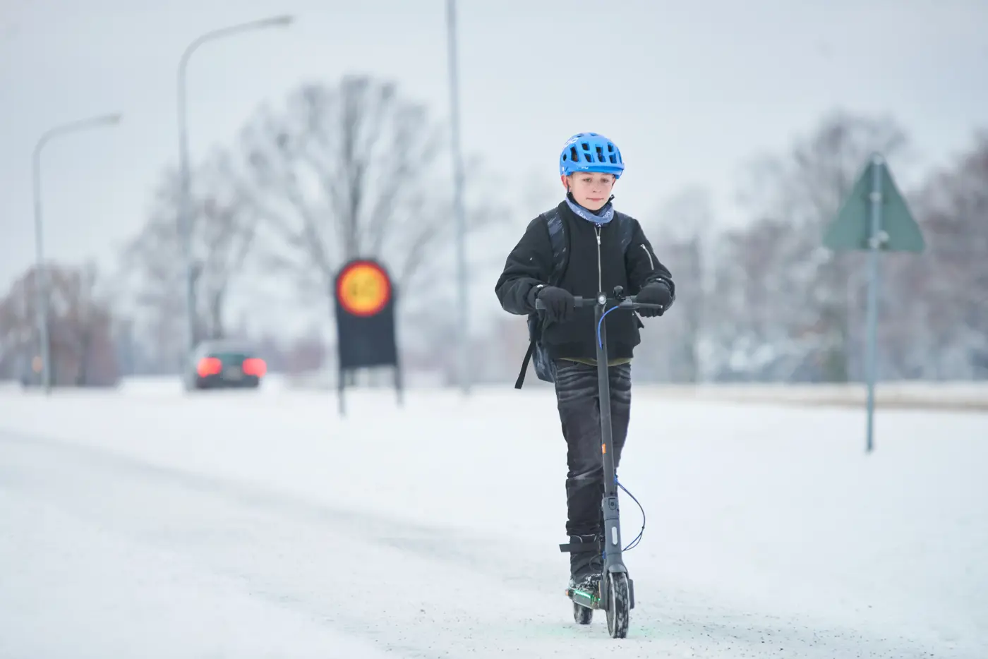 Kille med cykelhjälm som åker elsparkcykel under vintertid.