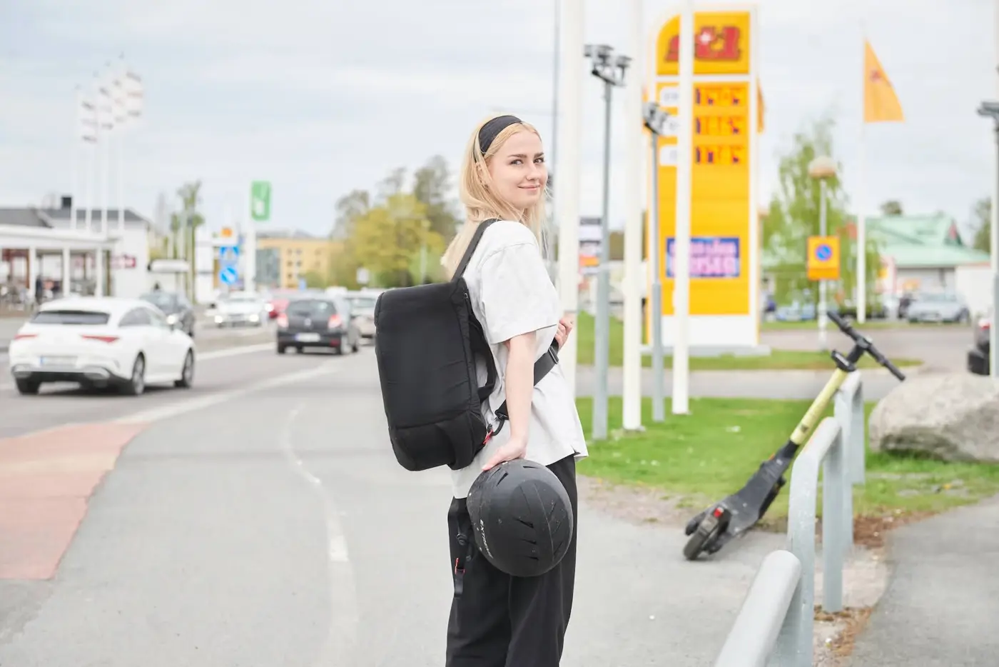 En tonåring står med en hjälm i handen framför en elsparkcykel.