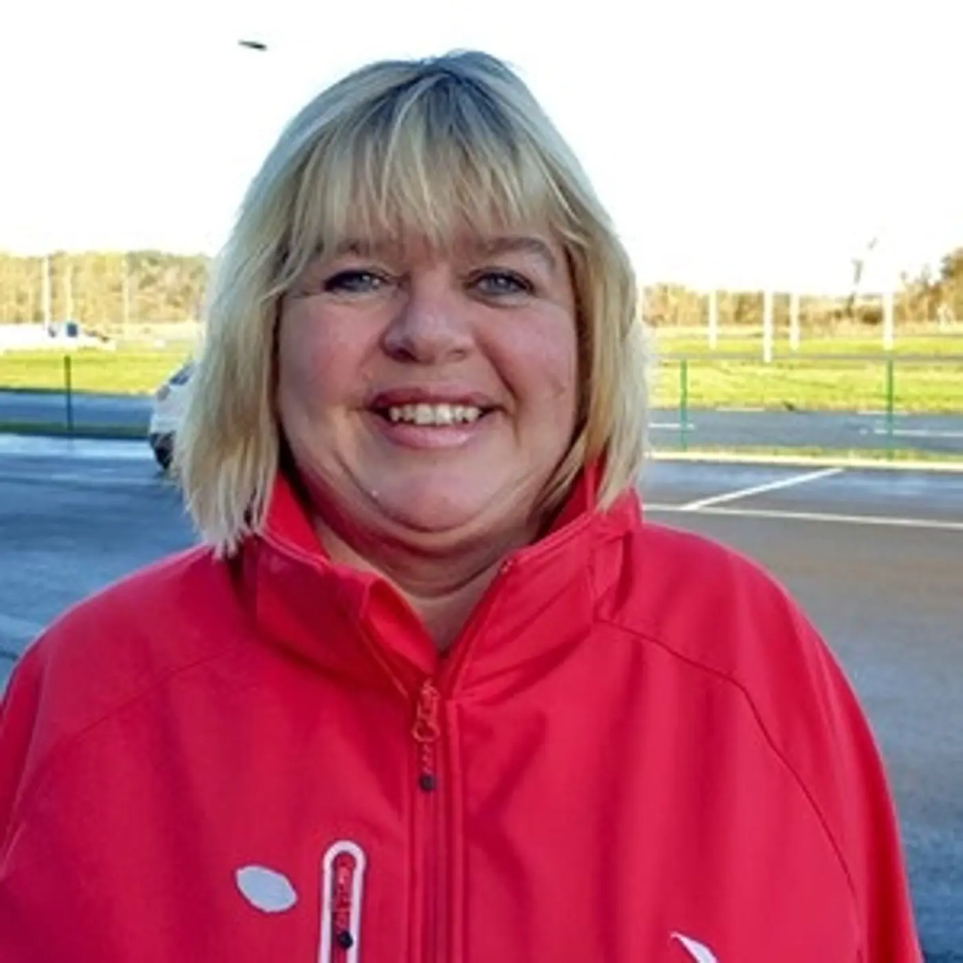 Porträttbild på en leende kvinna med axelkort hår och röd jacka.