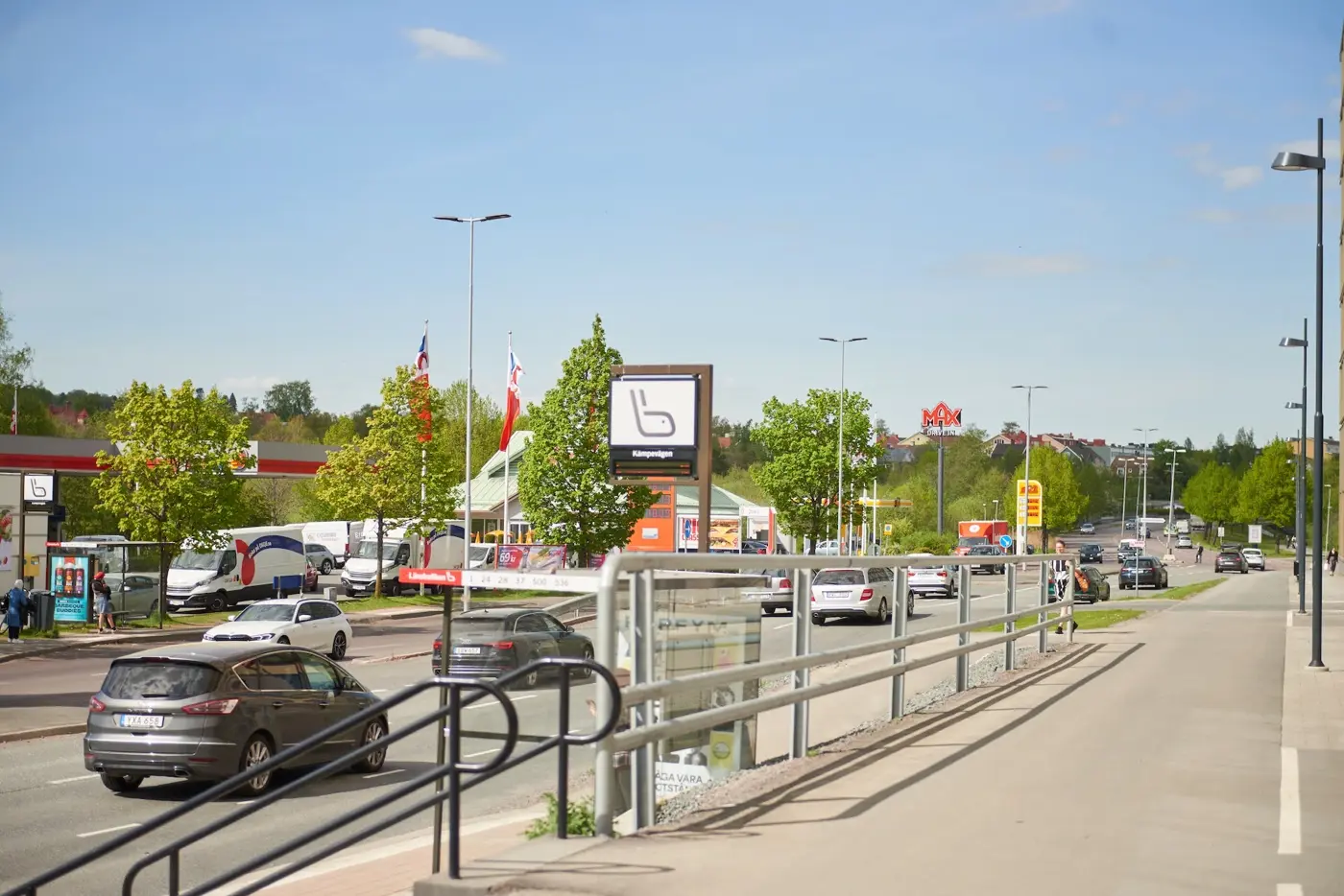 Bilar kör på en väg och till höger syns en busstation samt en gång-och cykelbana.