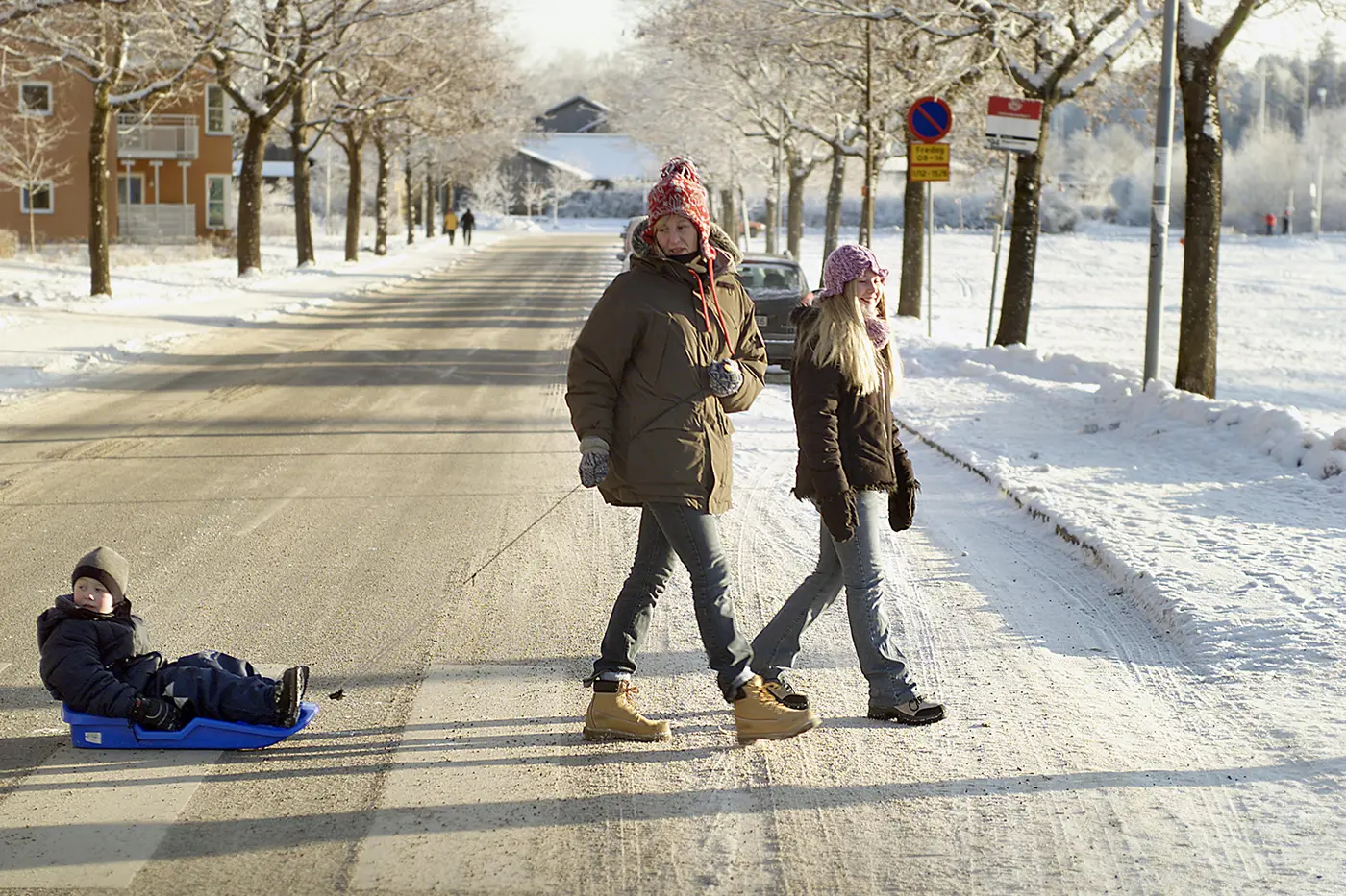 En förälder drar ett litet barn i en pulka över ett övergångsställe.