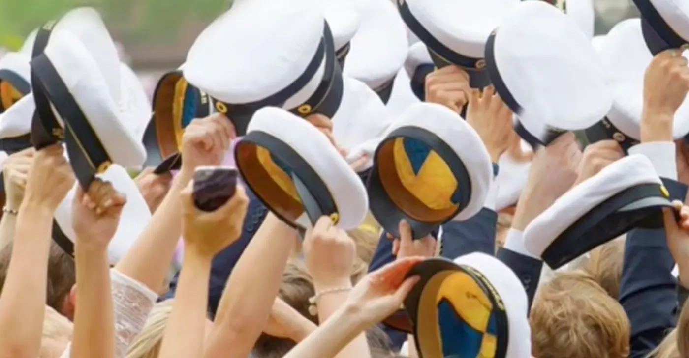 Studenter håller upp sina studentmössor.