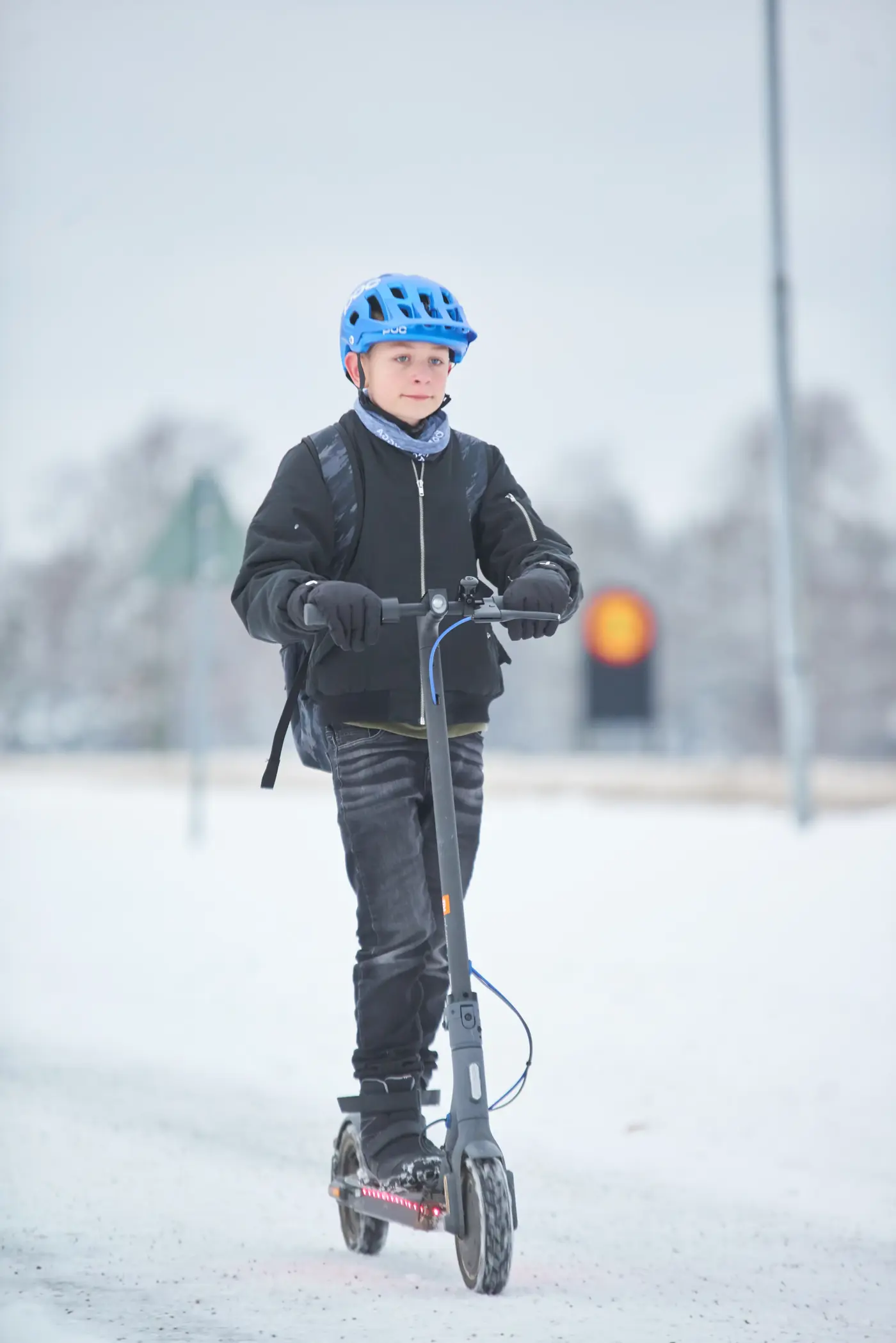 Kille med cykelhjälm som åker elsparkcykel under vintertid.