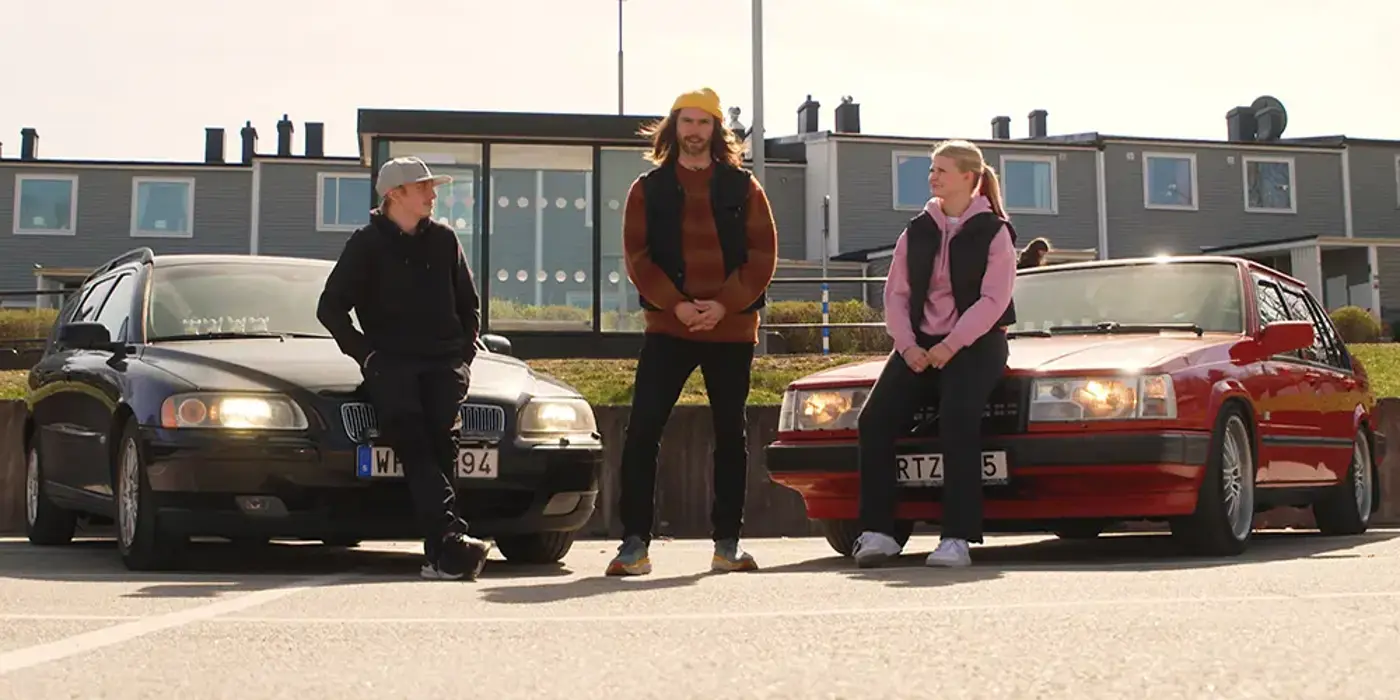 Tre ungdomar poserar framför två A-traktorer, en röd och en svart bil.