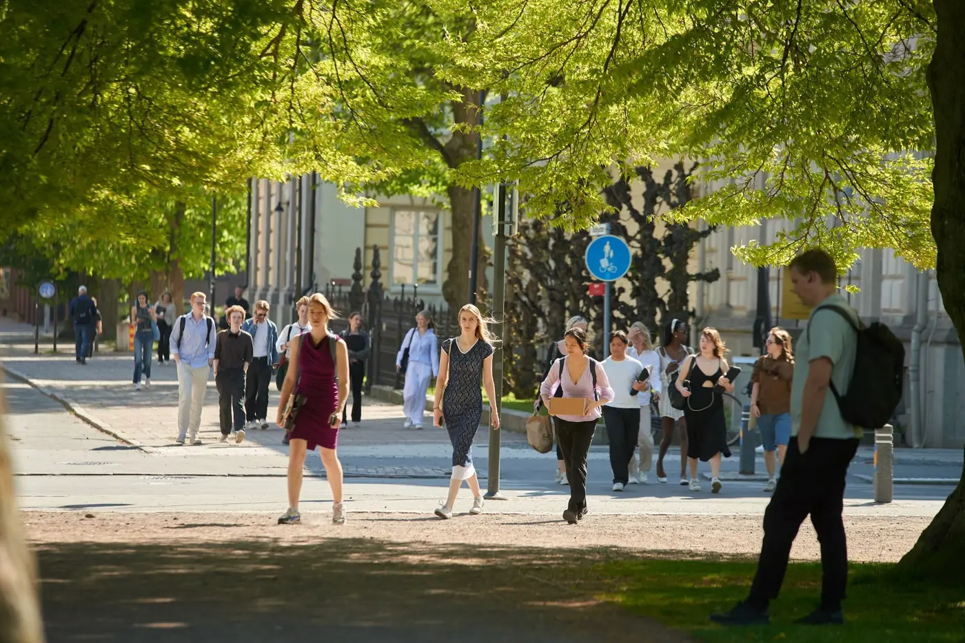 Människor i olika åldrar går på en gång- och cykelbana och korsar en väg vid en gångpassage.