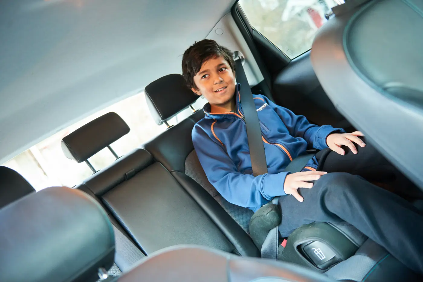 Ett barn sitter på en bälteskudde i baksätet med fastspänt bälte.