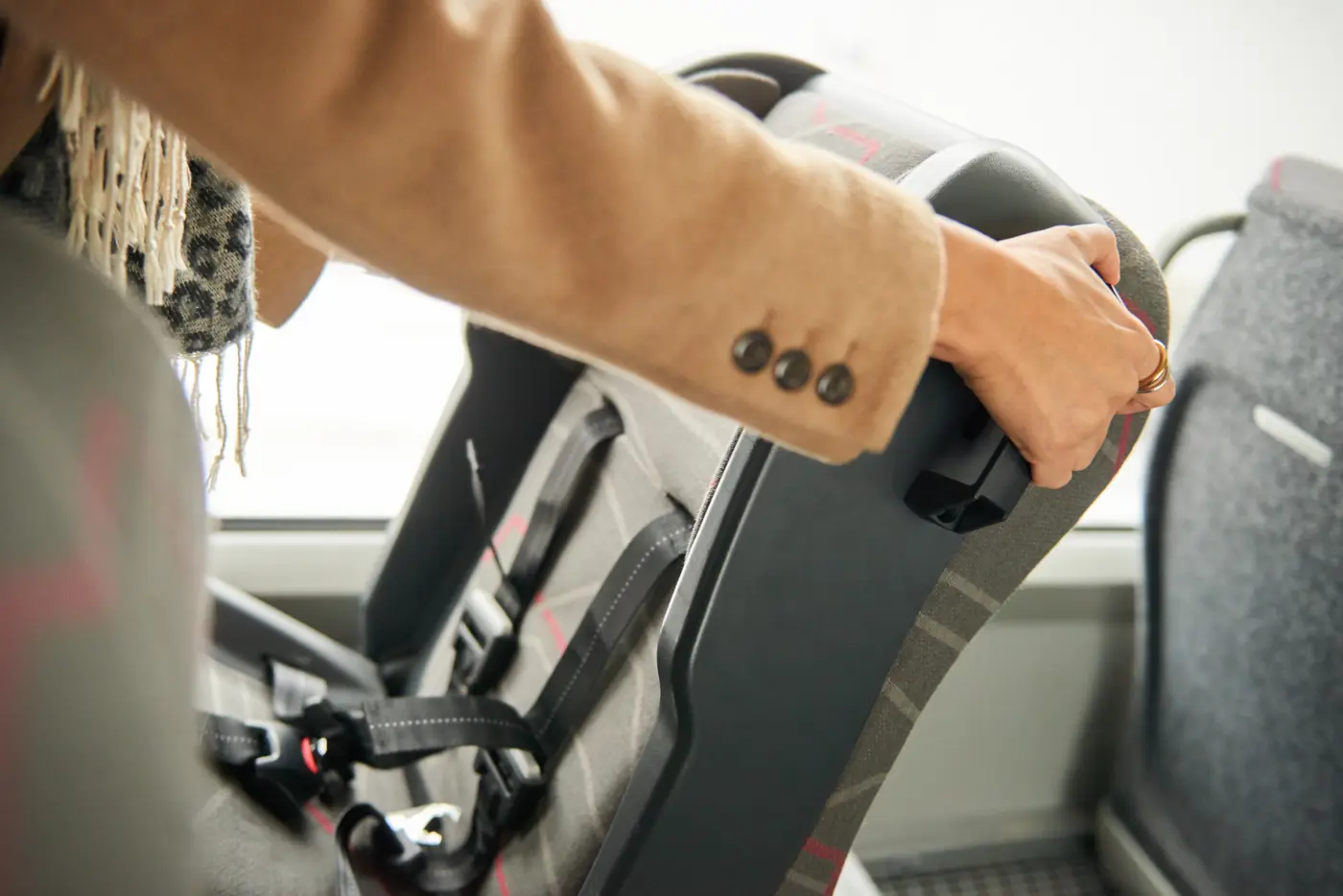 En förälder justerar en bakåtvänd bilbarnstol i en buss.