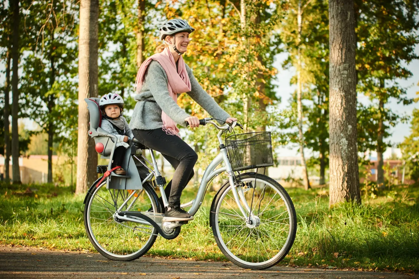 En mamma skjutsar sitt småbarn på cykel med hjälp av en cykelsits.